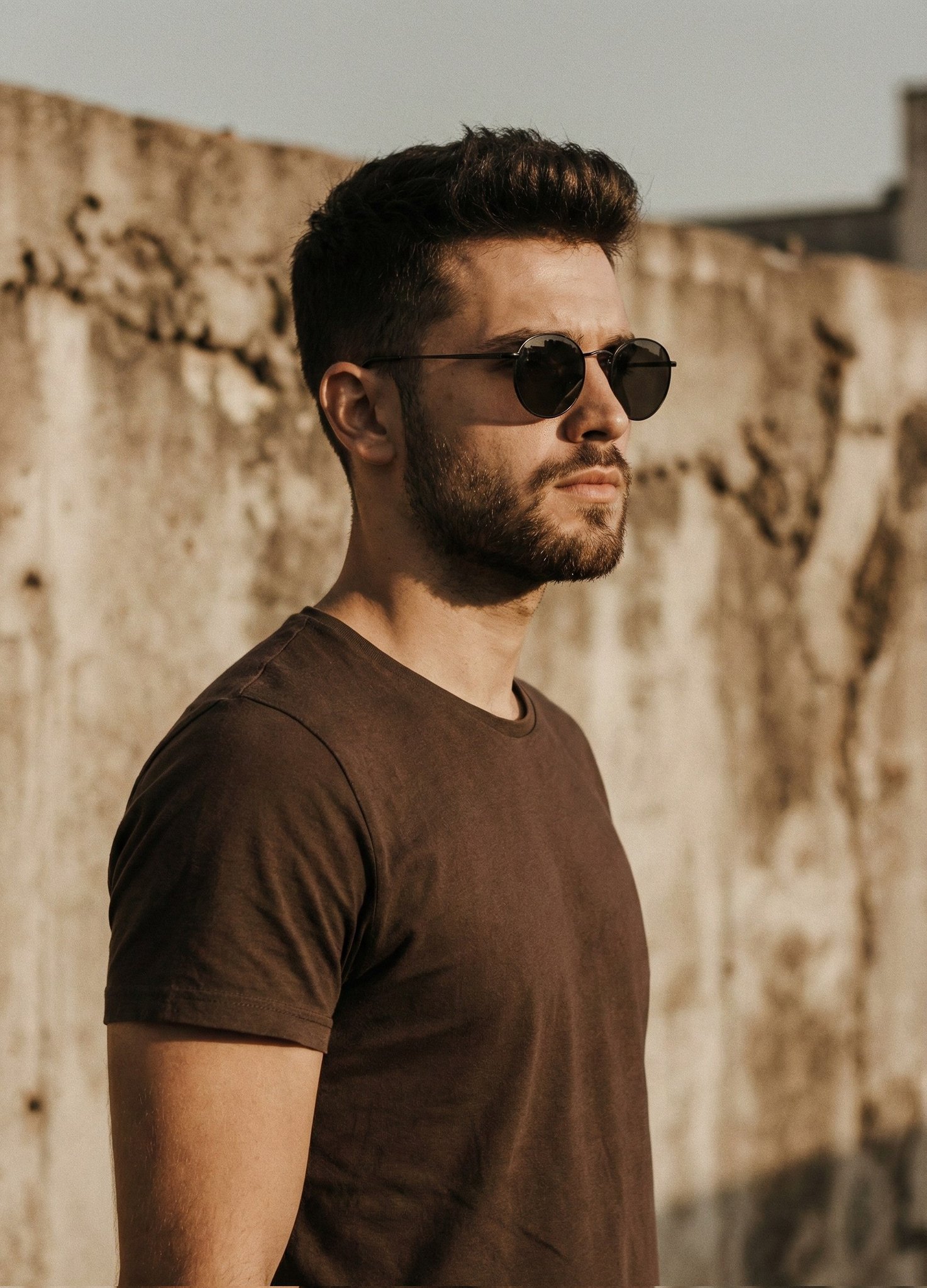 A cinematic portrait of a handsome man with a short styled haircut and trimmed beard, wearing a pla…