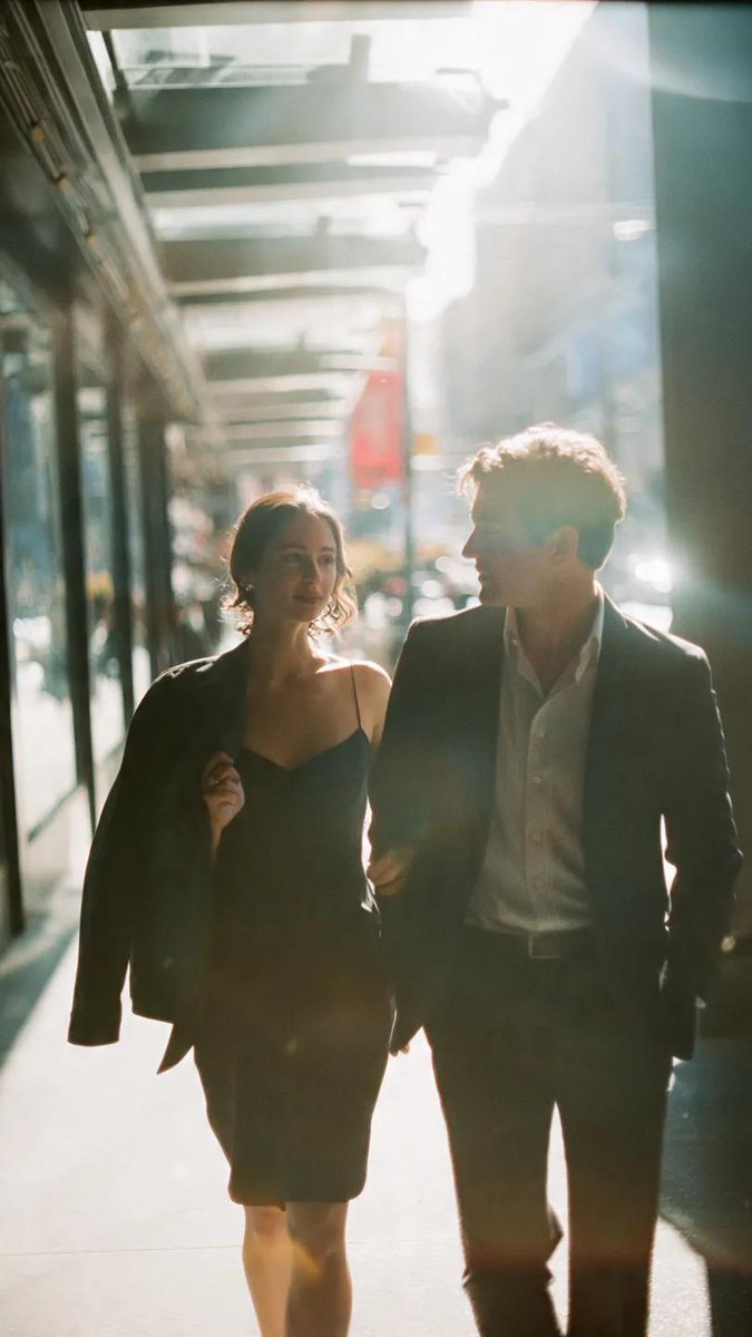 A cinematic candid medium shot portrait of a man and a woman walking side by side along a bright ur…