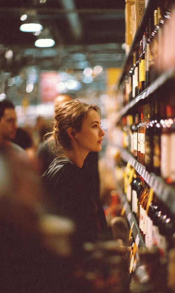 A cinematic side-profile portrait of a young woman standing in a grocery store aisle, carefully loo…